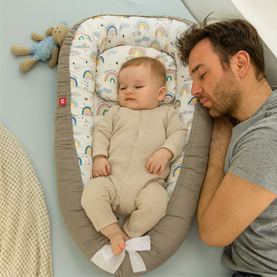 Bébé dort paisiblement dans cocon Bébé à côté papa NidPortableBebe Arc-En-Ciel