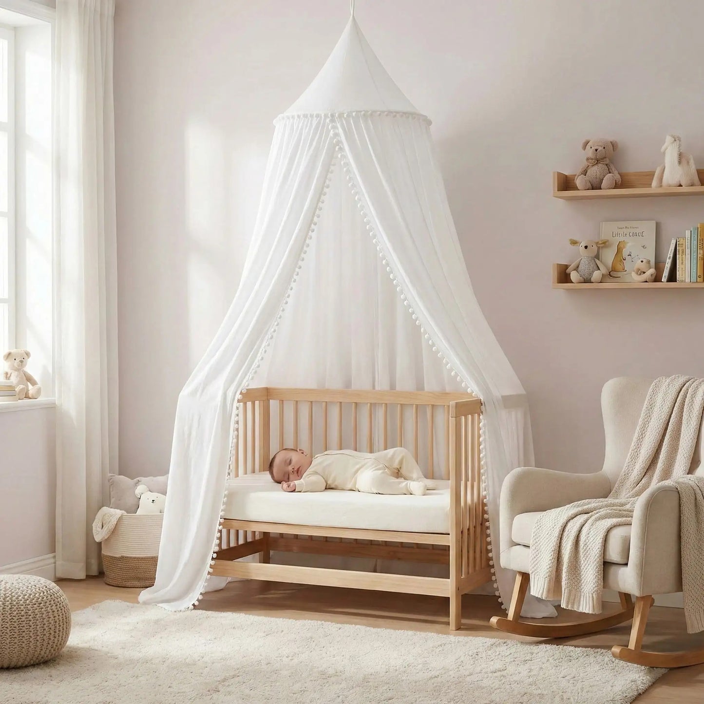Bébé dort paisiblement sous un ciel de lit blanc bebe avec pompons dans un berceau en bois Cocon Protecteur