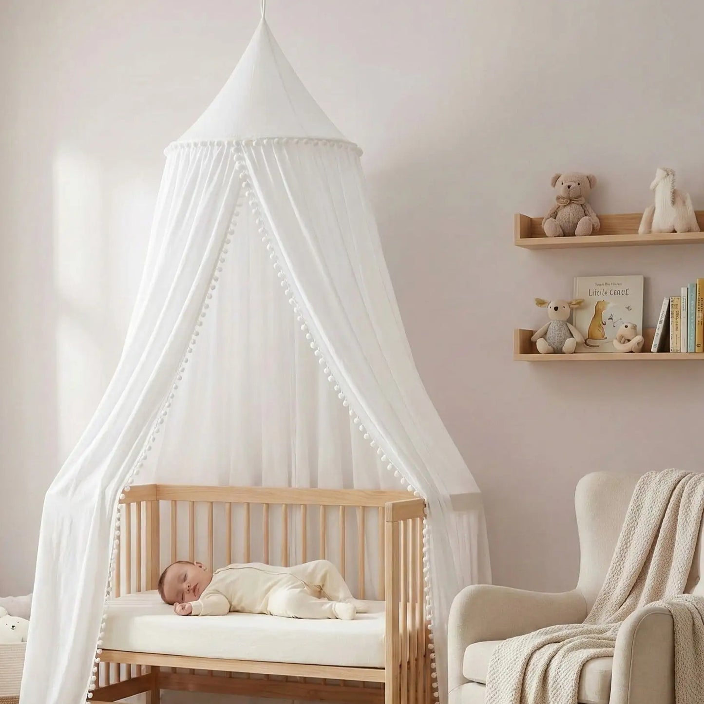 Bébé dort sereinement sous un ciel de lit blanc bebe avec pompons dans un berceau en bois Cocon Protecteur