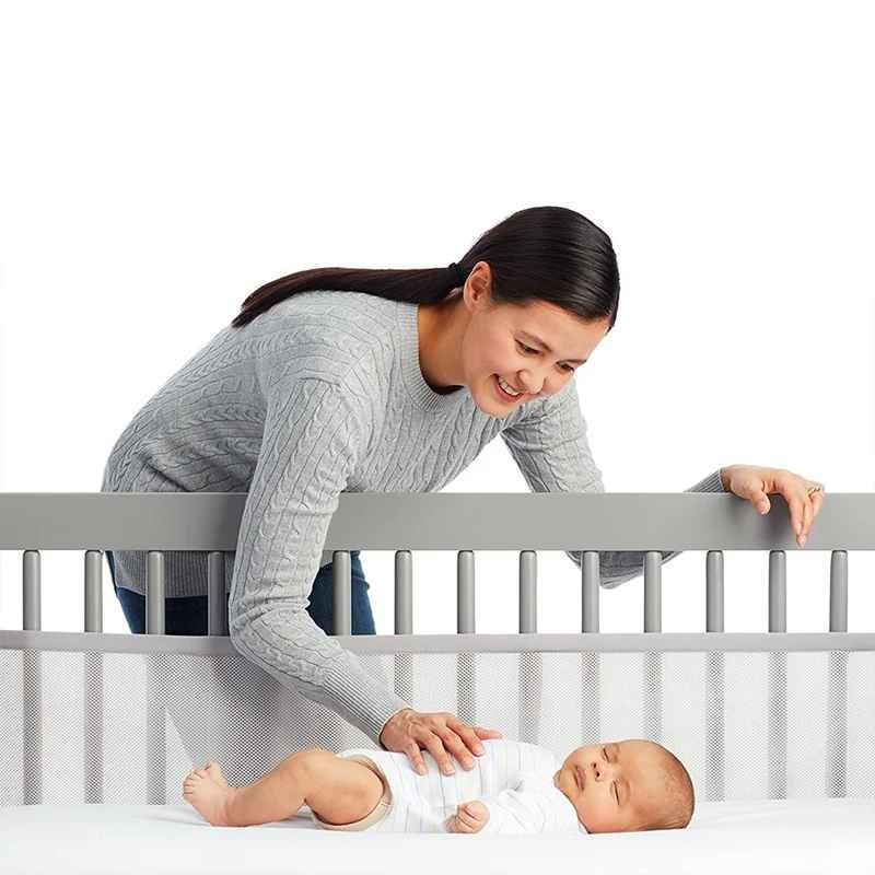 Maman caresse bébé qui dort paisiblement dans berceau avce tour de lit respirant AirSafe
